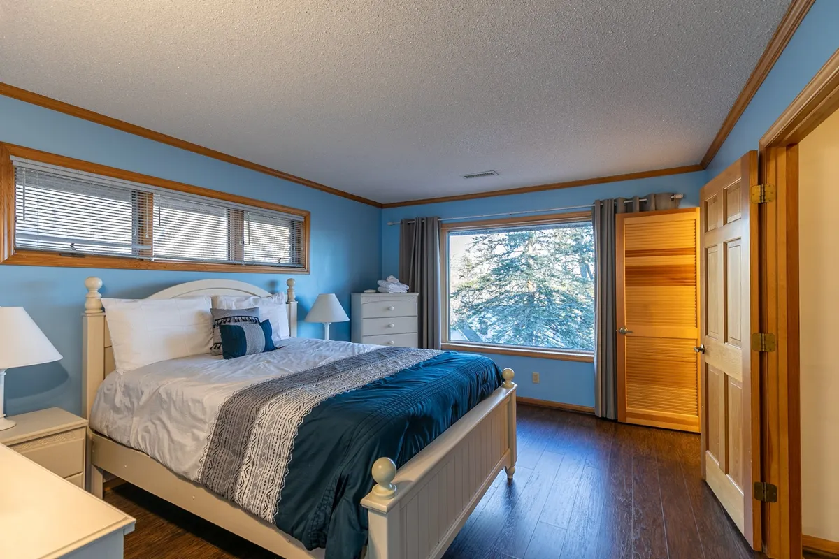 A tranquil bedroom with a large window offering peaceful views of the trees, a comfortable bed adorned with decorative pillows, and classic wooden furniture for a restful atmosphere.