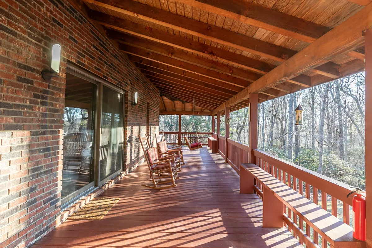 A peaceful exterior scene featuring rocking chairs on a wooden deck, overlooking a backdrop of trees. The inviting space suggests a perfect spot for enjoying mountain air, storytelling, and soaking up nature in a serene environment.