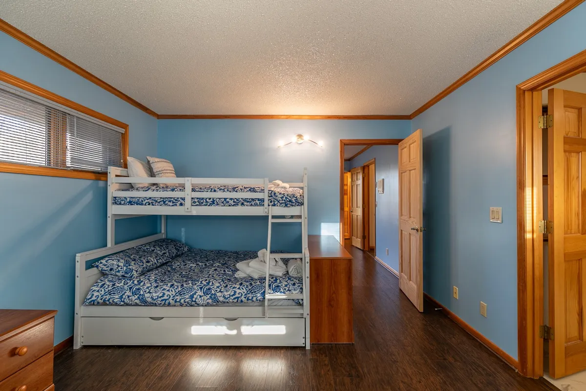 A cheerful room with sturdy wooden bunk beds set against blue walls, complemented by additional wooden furniture. Soft lighting and a cozy atmosphere make this an inviting space for children.