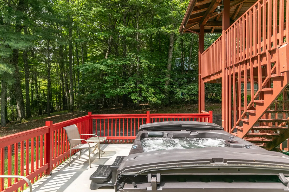 A tranquil view of the hot tub nestled on the deck, surrounded by red railing and lush forest. The hot tub sits in an inviting position, offering privacy and a scenic natural backdrop.