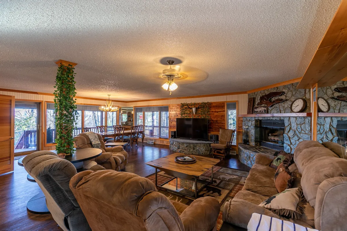 A spacious living area drenched in natural light, featuring large windows that frame scenic mountain views, a cozy stone fireplace with comfortable seating, and a dining space ideal for family meals or remote work.