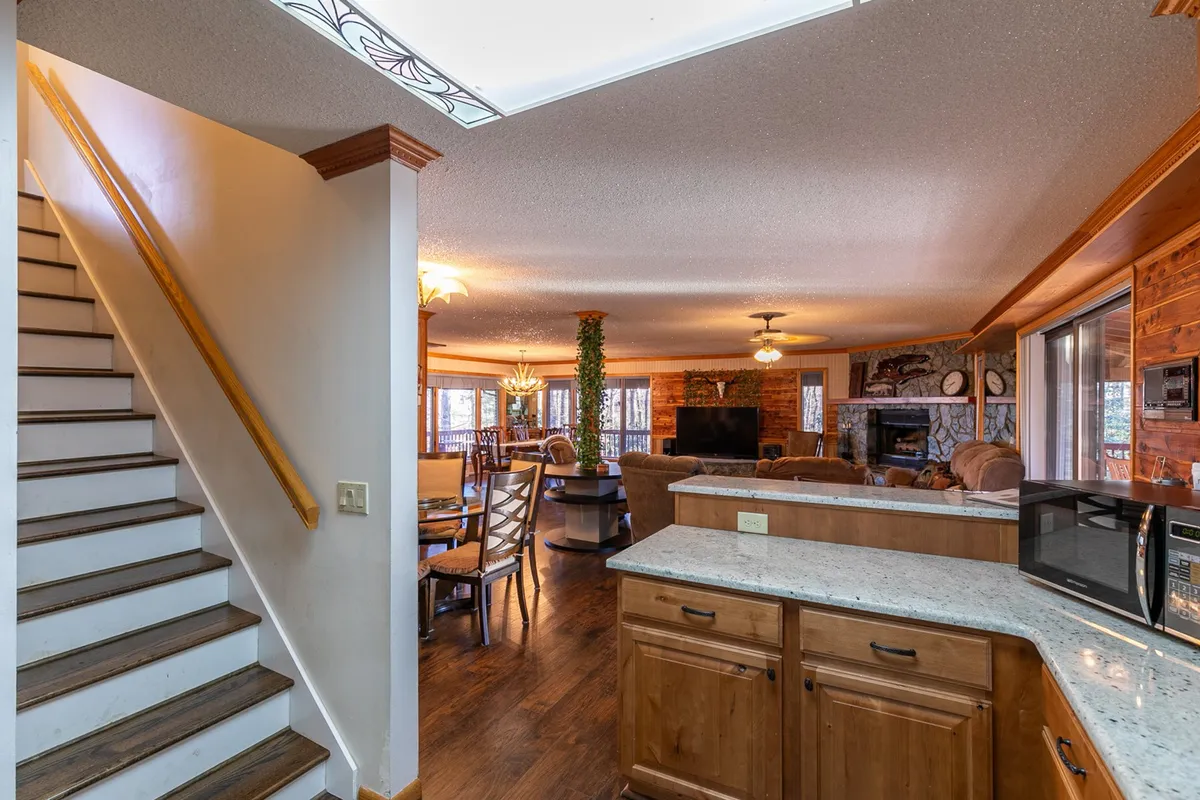 An inviting open-concept space with a visible kitchen, dining area, and living room anchored by a stone fireplace—the heart of daily life. The scene suggests easy movement between cooking, dining, and relaxing, embodying home comforts for long-term guests.
