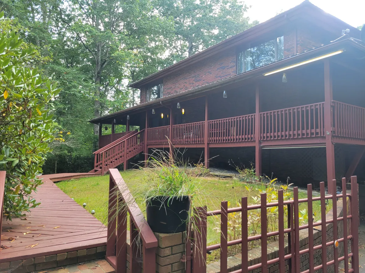 A welcoming exterior view of the property’s wooden walkway leading to a brick facade and porch adorned with hanging lights. The scene hints at gatherings, warm welcomes, and the anticipation of adventures just beyond the doorstep.
