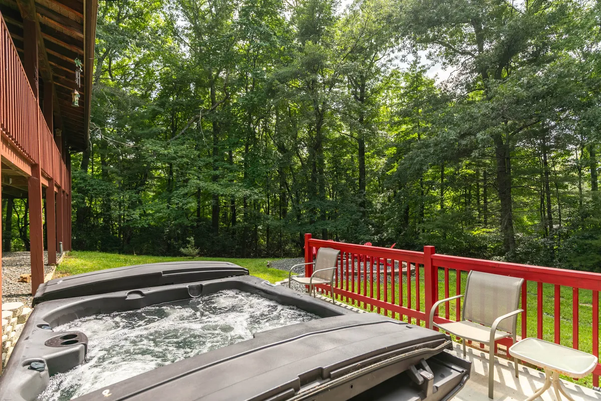 This image showcases a tranquil hot tub nestled on a wooden deck, bordered by a striking red railing and surrounded by lush greenery. The natural setting emphasizes relaxation and immersion in nature after a day of outdoor adventure.