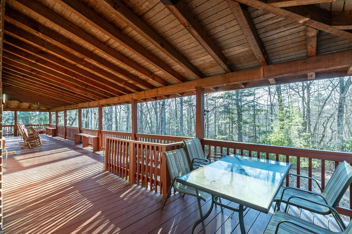 This image showcases a spacious wooden deck with a dining table, rocking chairs, and abundant surrounding trees. The seating arrangement invites outdoor dining and gathering while providing immersive views of nature.